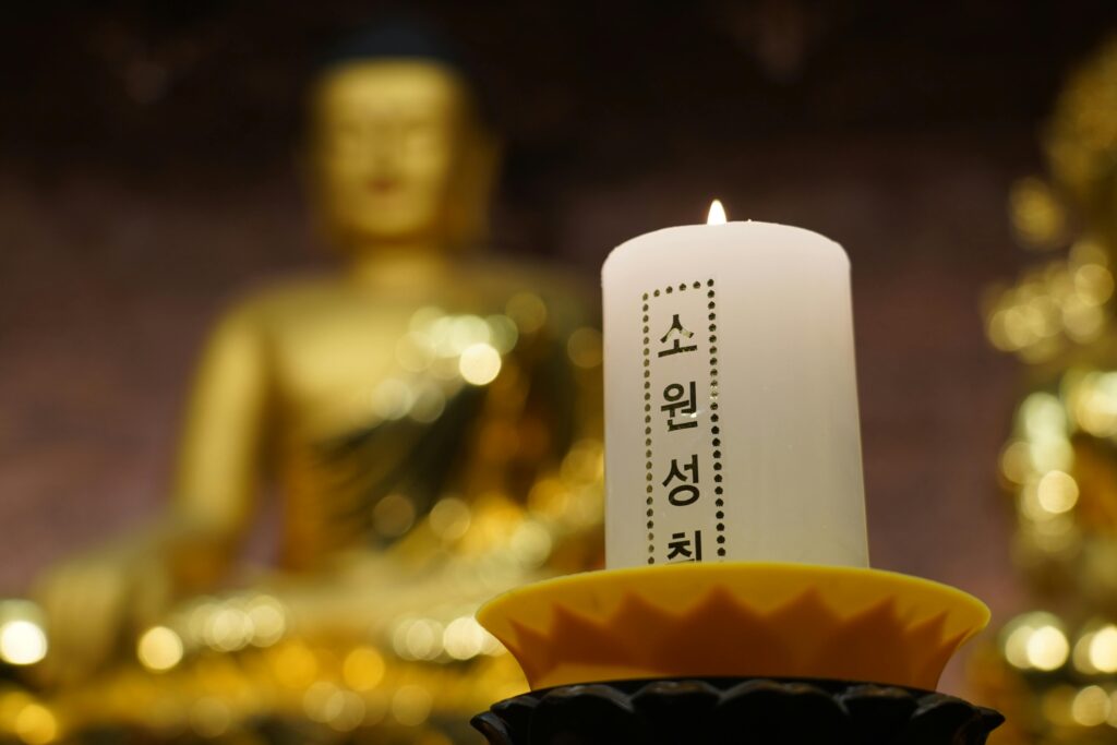 A single candle glows with Buddha statue in a Seoul temple background.